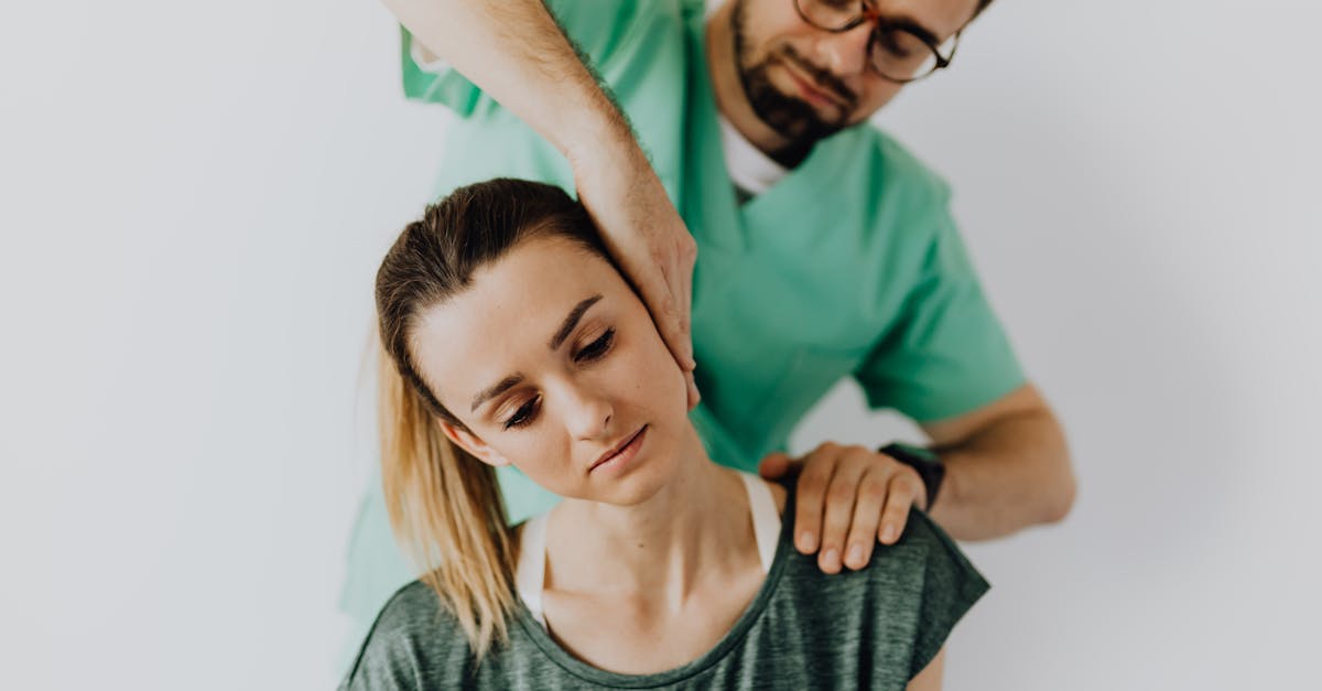 Concentrated doctor massage therapist in medical uniform doing therapeutic neck massage for calm young female patient in casual wear