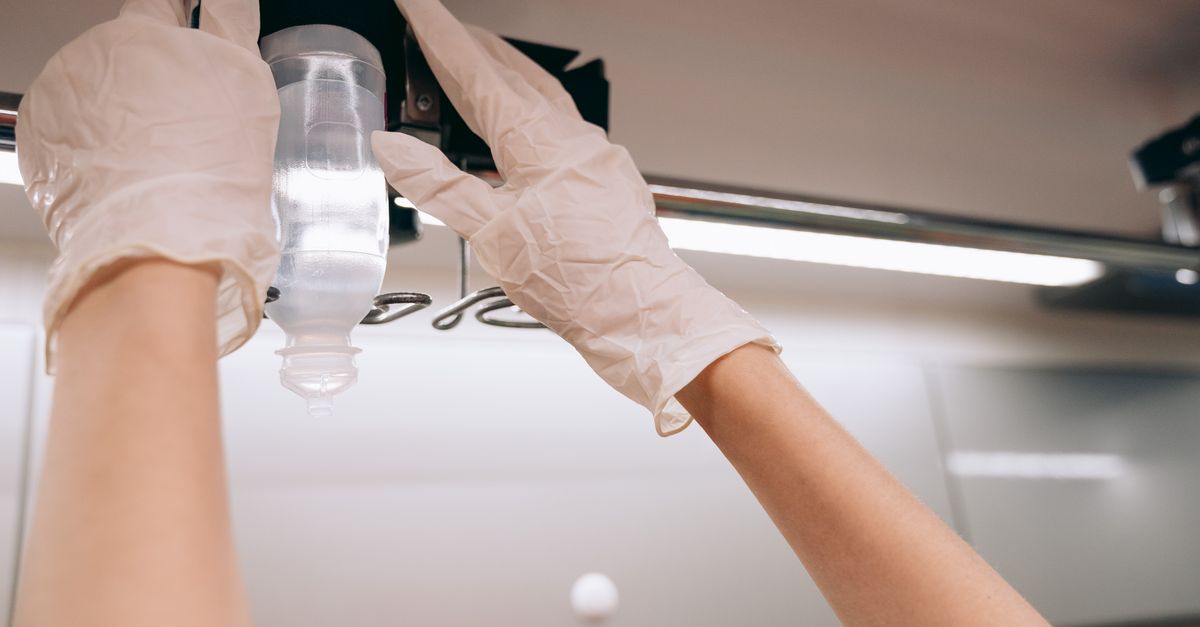 Close-up of gloved hands adjusting an IV drip in a clinical setting, emphasizing healthcare professionalism.