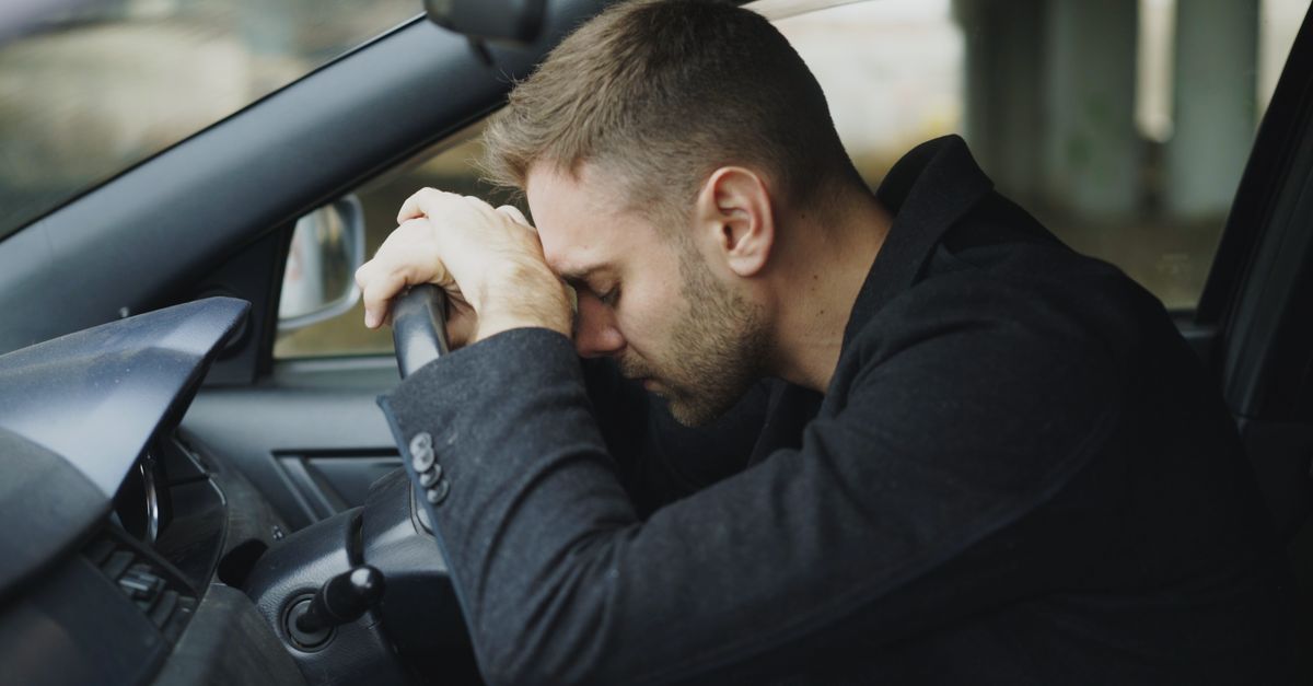 A man showing stress while sitting in a car, head on steering wheel.