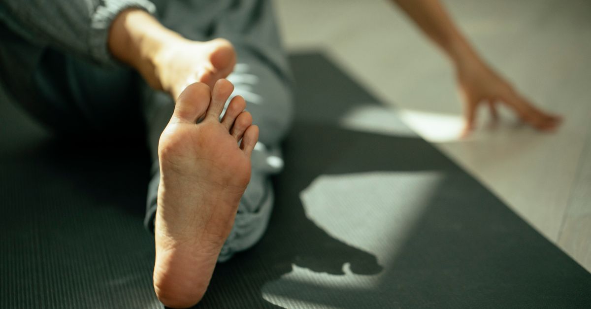 Crop anonymous barefoot woman in sportswear sitting on mat stretching legs during yoga session in studio