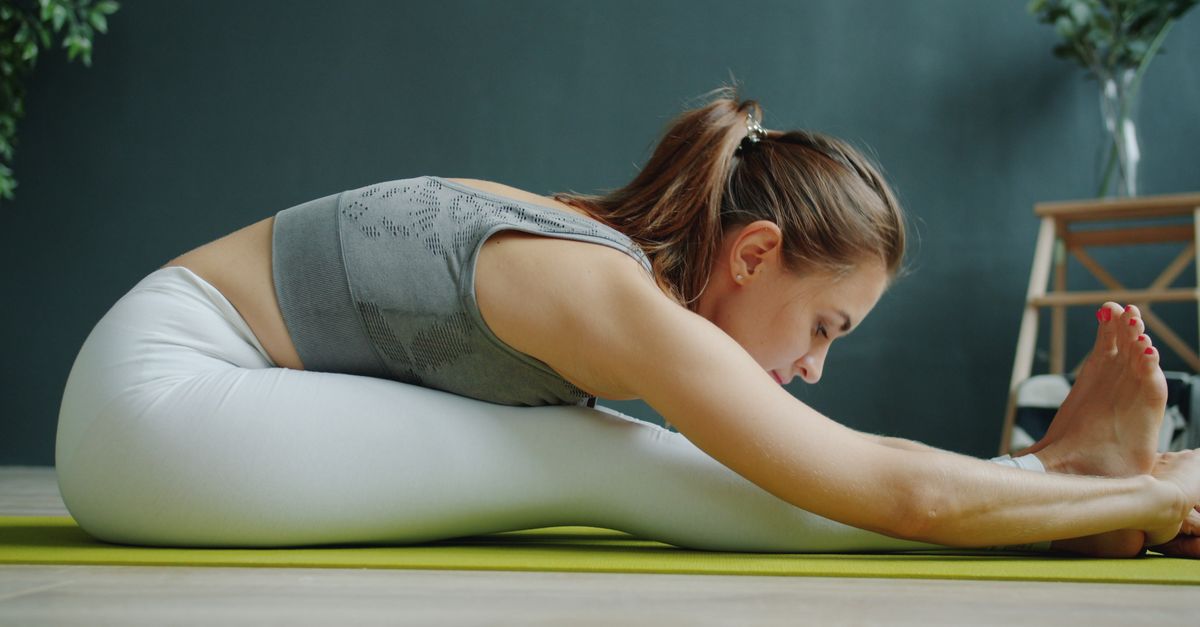 A woman in activewear stretching on a yoga mat indoors, focusing on wellness and fitness.