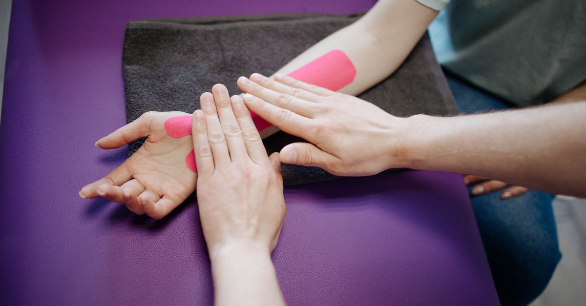 Close-up of hands applying pink kinesiology tape during a relaxing arm massage.