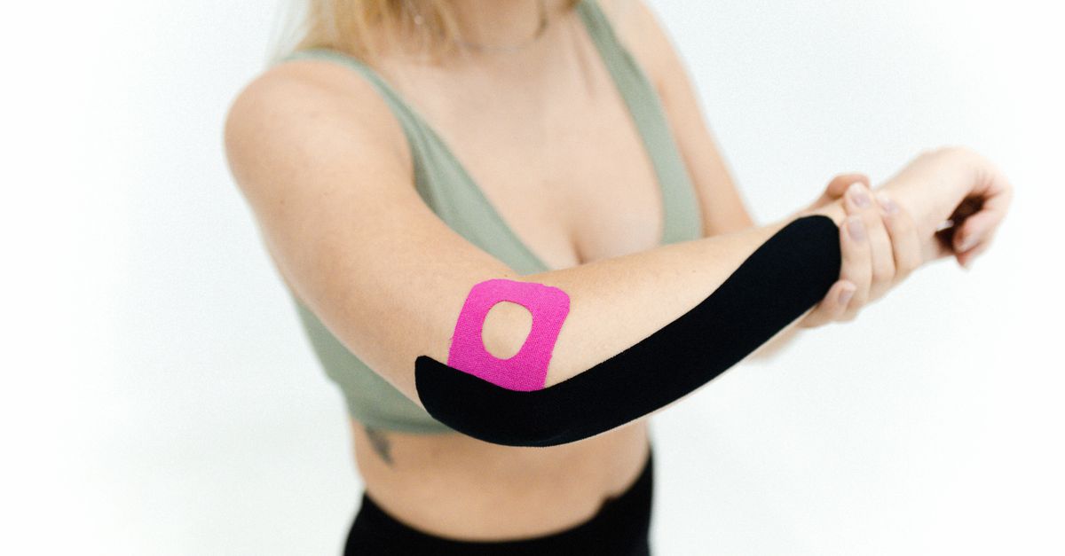Close-up of a woman applying kinesio tape on her arm for therapeutic treatment on a white background.