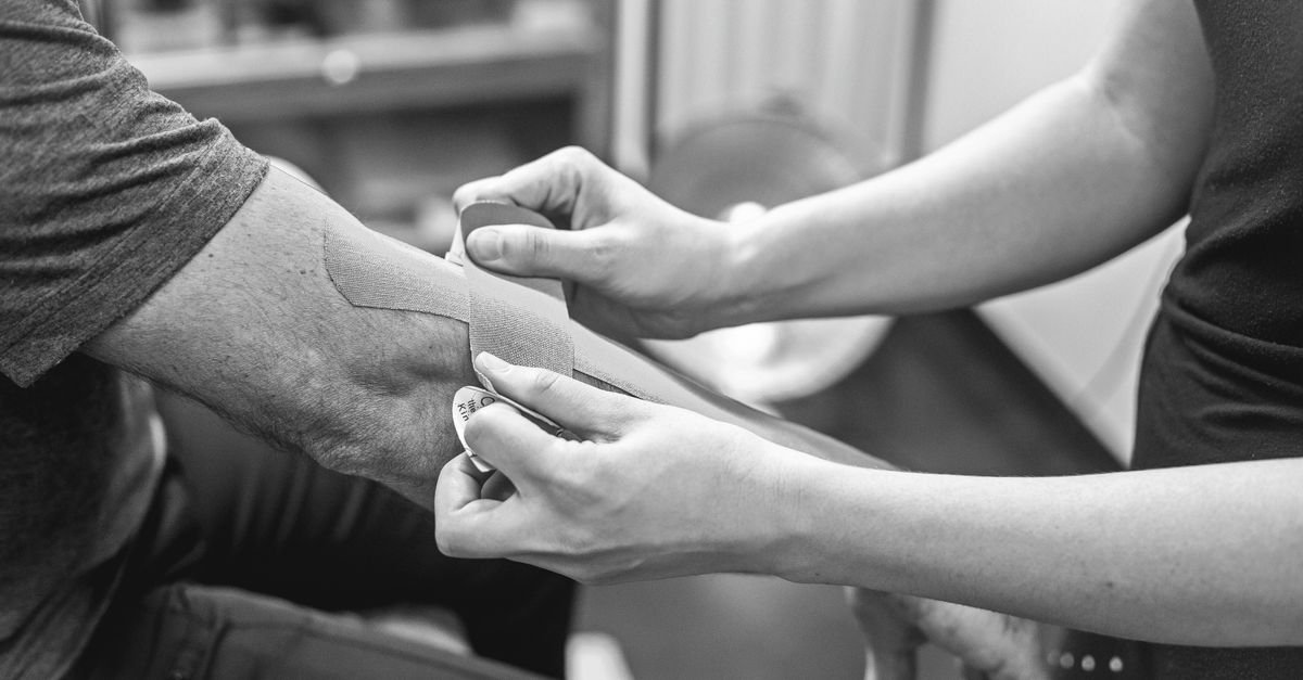 Close-up of kinesiology tape being applied on an elbow for therapeutic support in a healthcare setting.